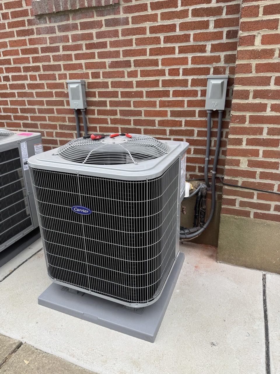 New Carrier outdoor condenser installed on a pad beside a brick house