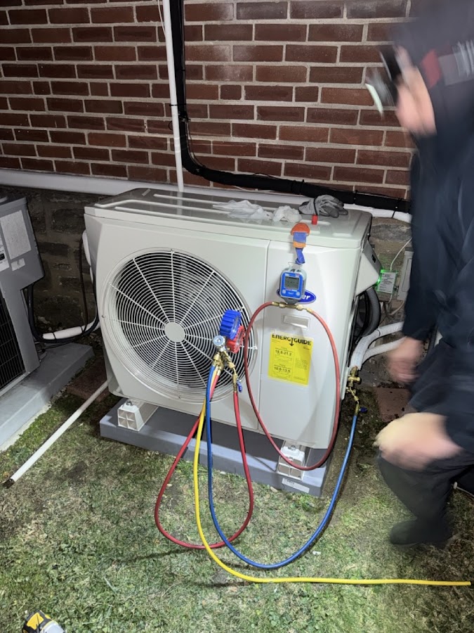 Technician with gauge hoses connected to a white ductless outdoor unit